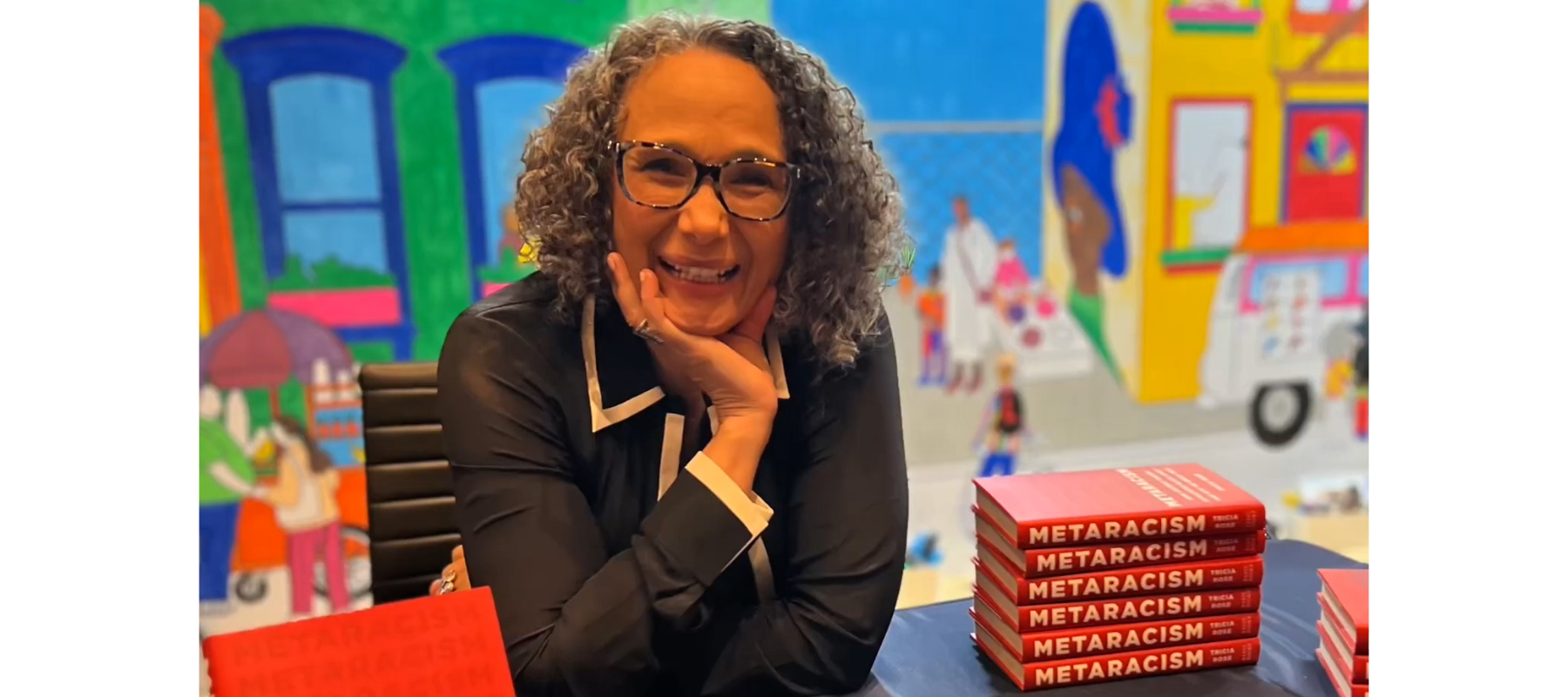 Professor and author Tricia Rose smiles next to a stack of her latest book Metaracism