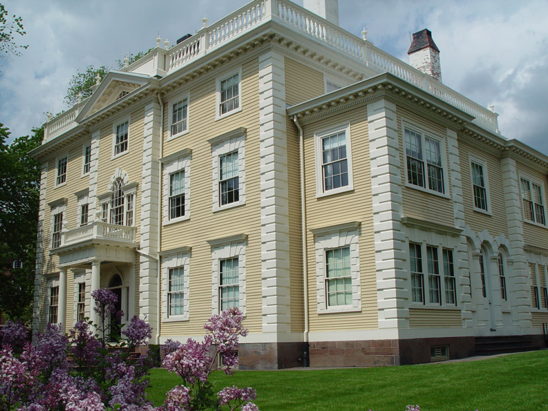 exterior view of a large victorian mansion with yellow walls and white trim