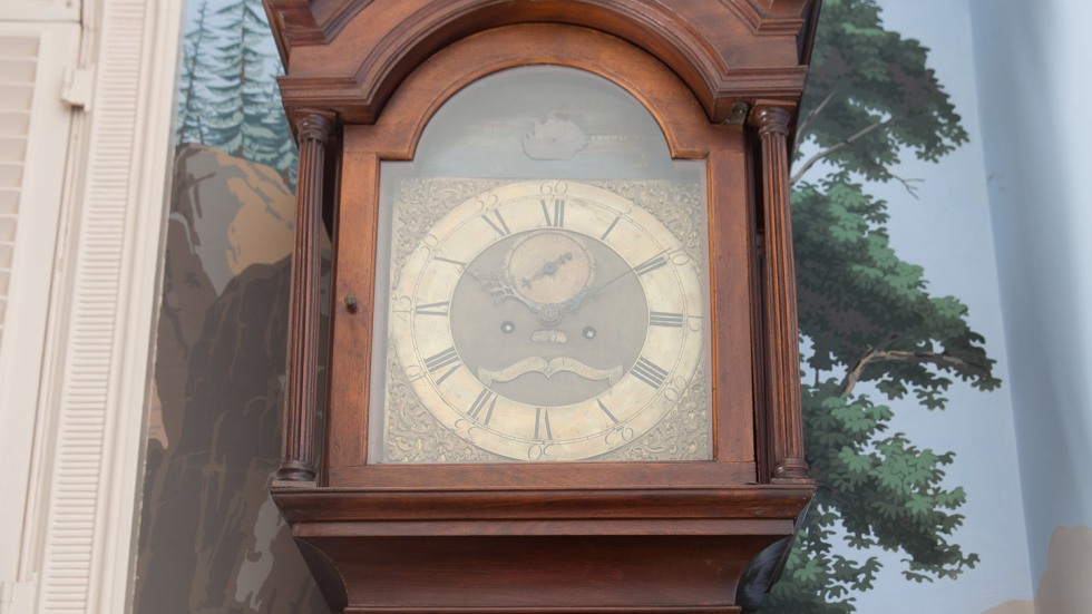 grandfather clock in front of a wallpapered wall