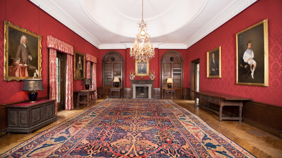 long view of a large red room with red walls, central chandelier and large colorful rug